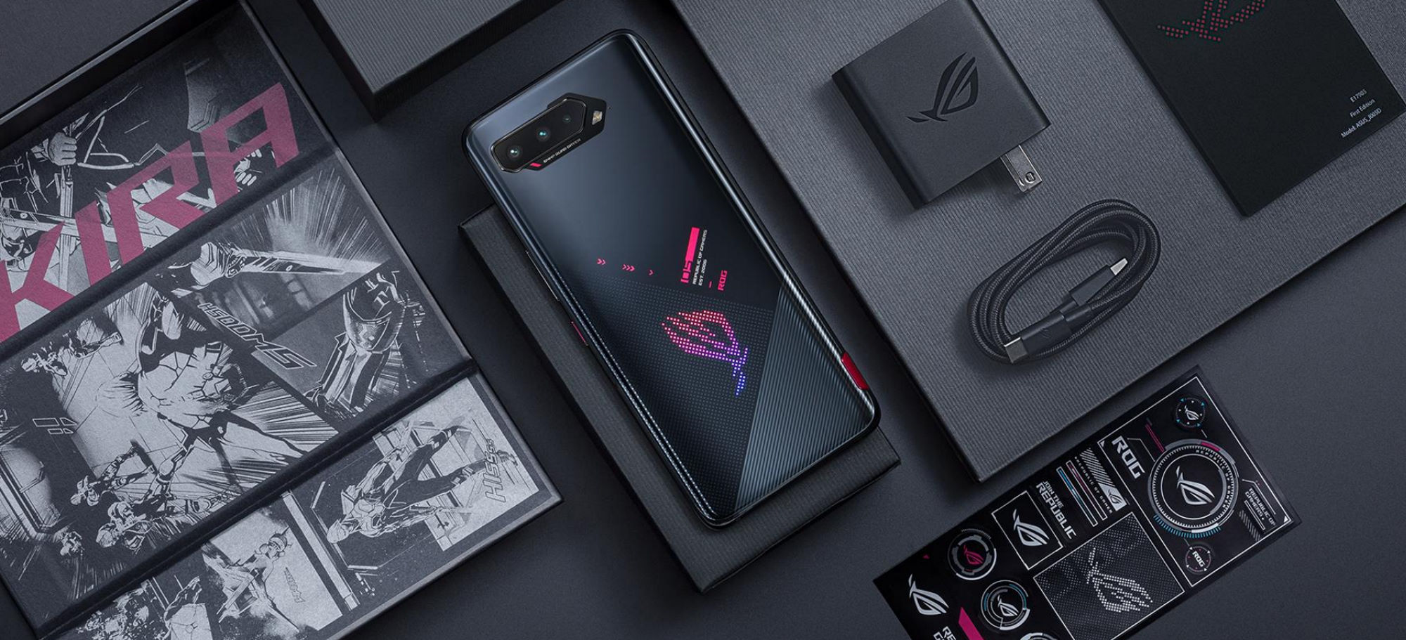 ROG Phone 5 on a black table, laid out next to the package contents like a battery charger and stickers.