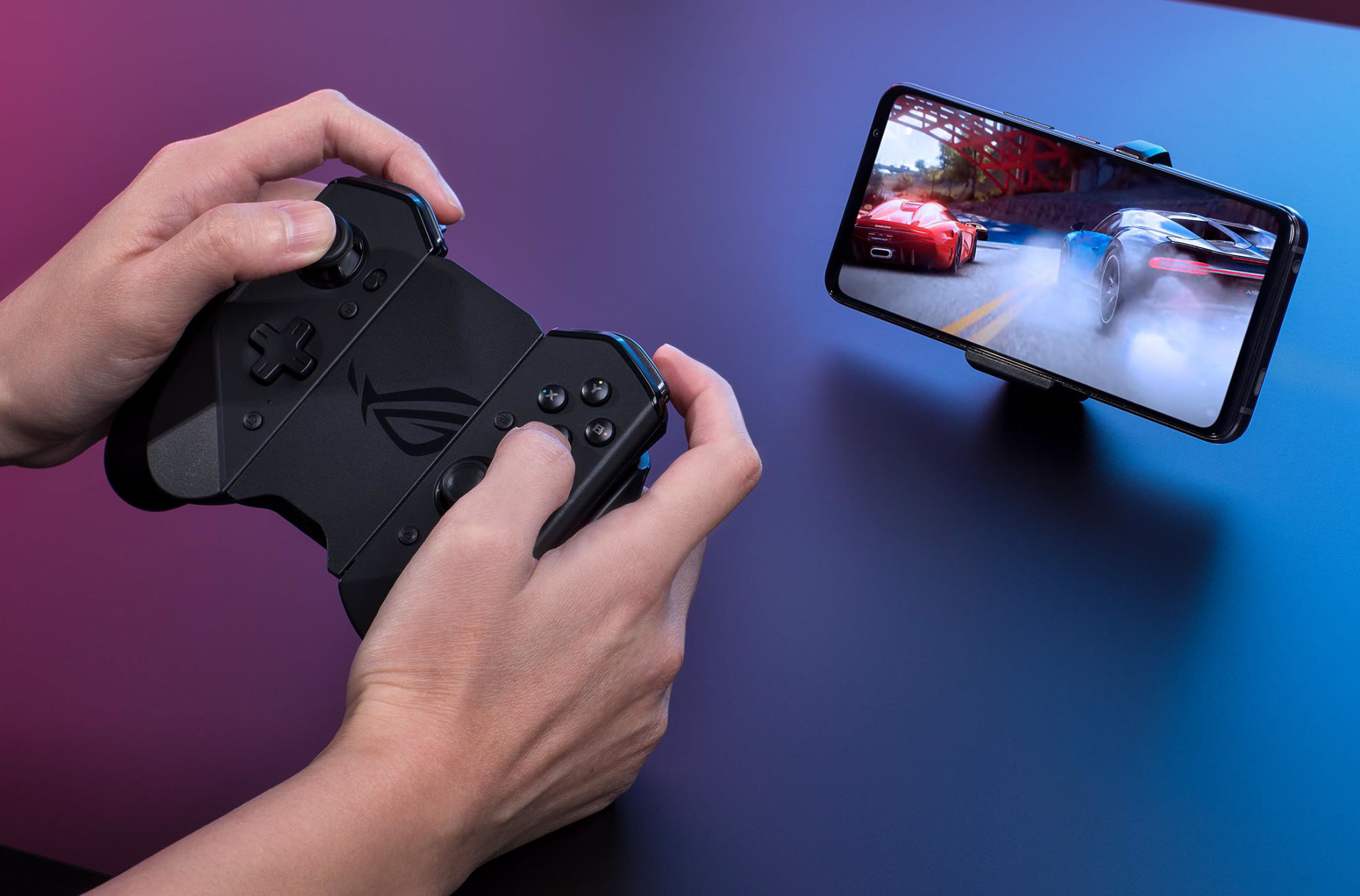 Image of a gamer holding the Kunai 3 gamepad to compete in a racing game, with the phone sitting on a table.