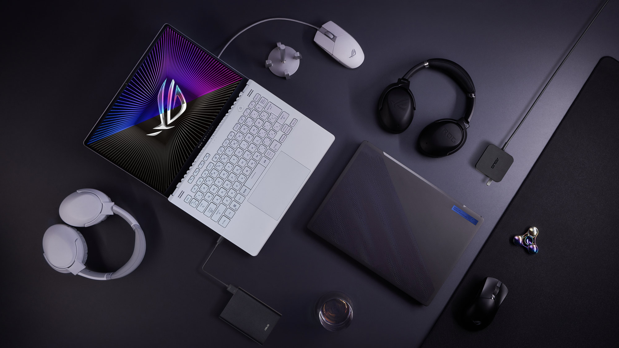 A photo of the Zephyrus G14 laptop laid out on a table, surrounded by headphones, mice, and other peripherals.
