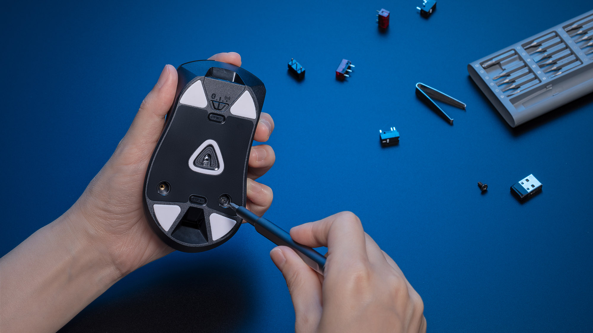 A photo of a hand unscrewing the screws on the bottom of a gaming mouse.
