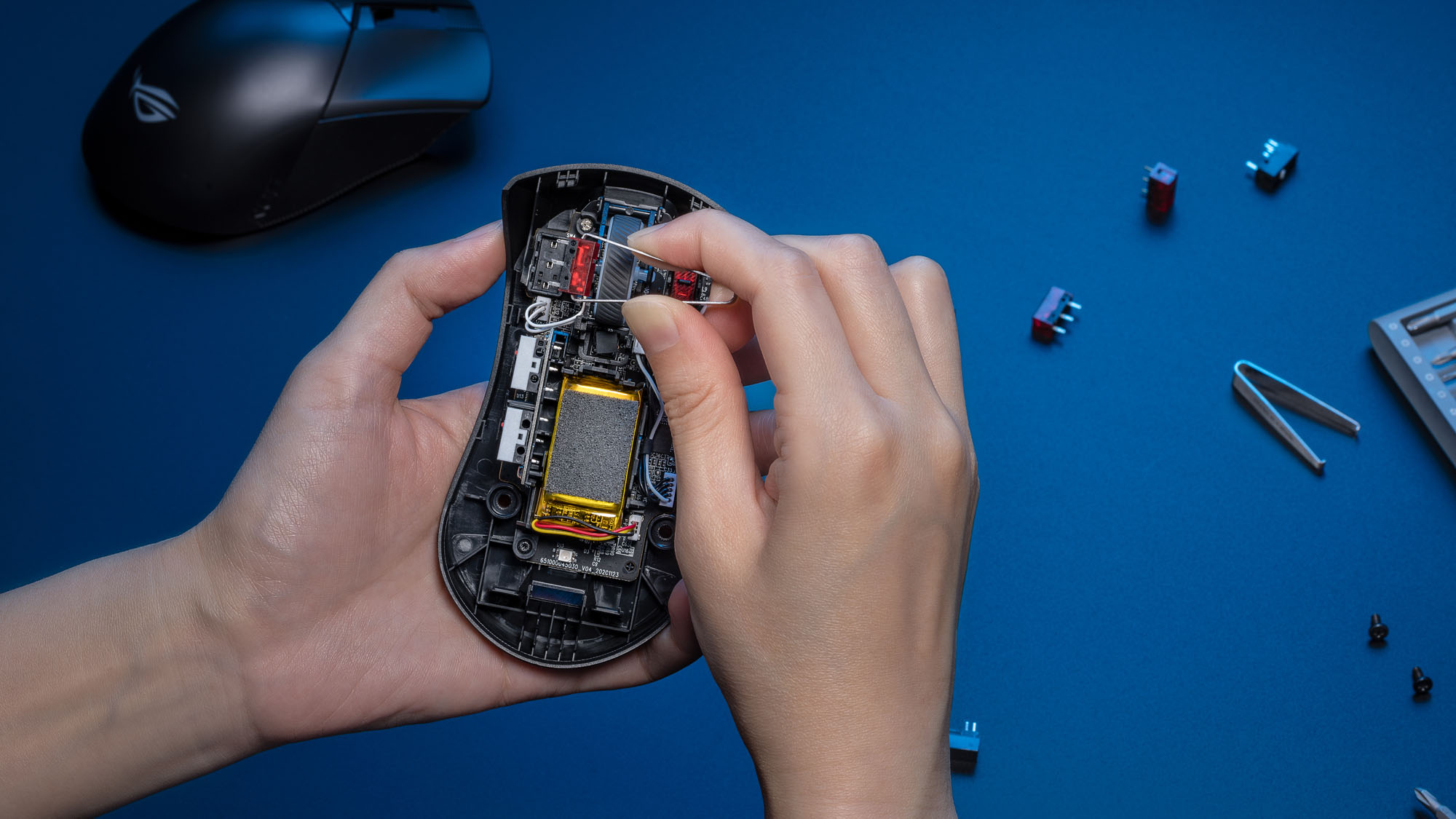 A photo showing the removal of a mouse switch using a pair of tweezers.