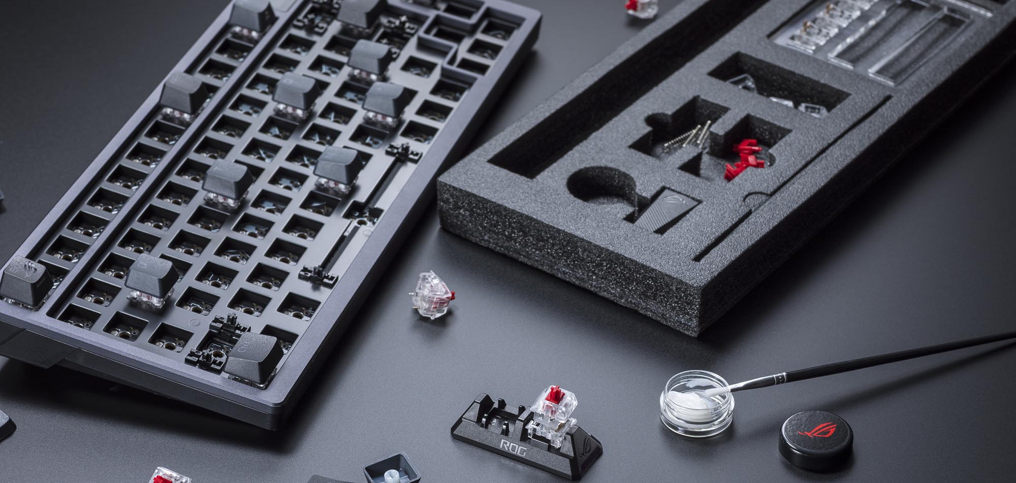 A disassembled ROG Azoth keyboard next to a brush dipped in switch lubricant.
