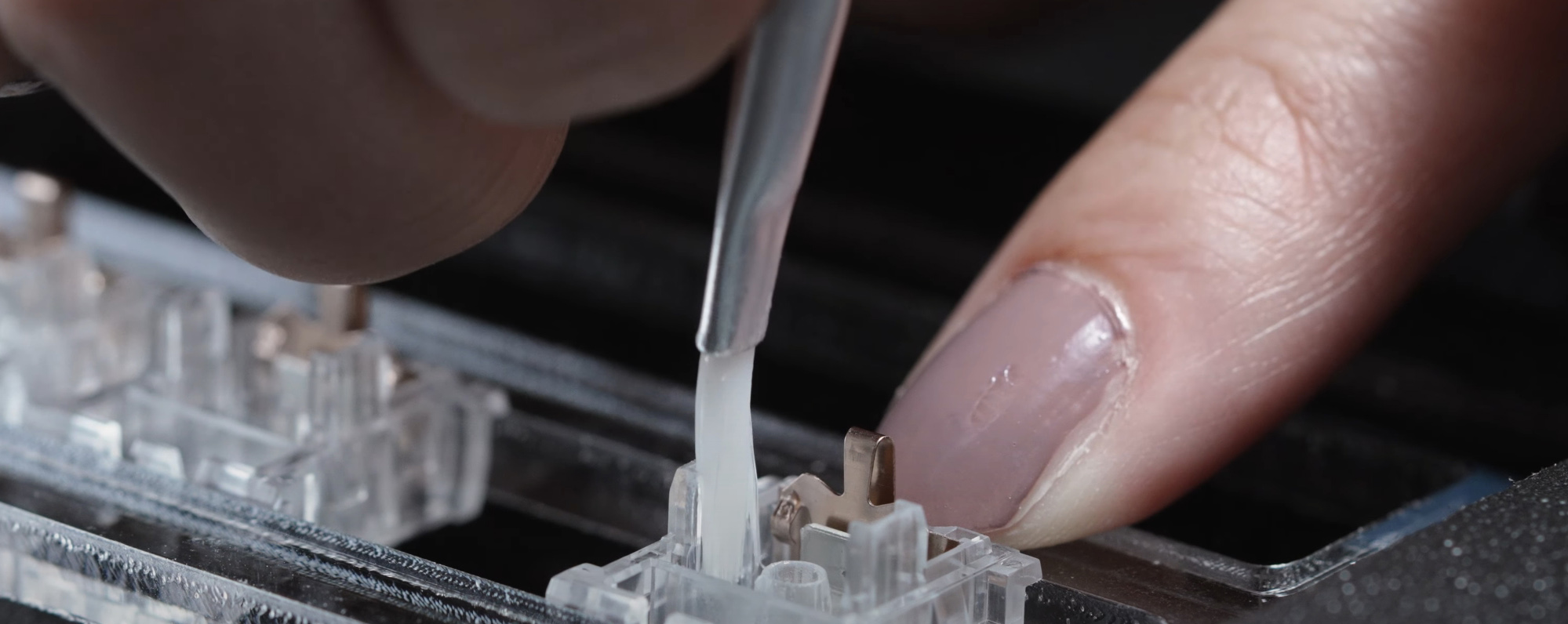 A paintbrush brushing against the sides of an opened keyboard switch housing.