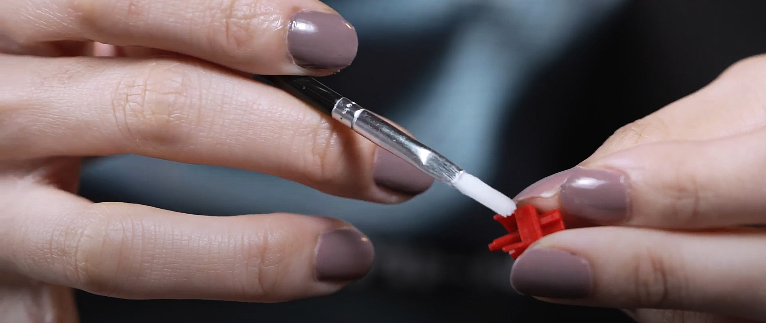 A hand holding a paintbrush against a red keyboard switch stem.