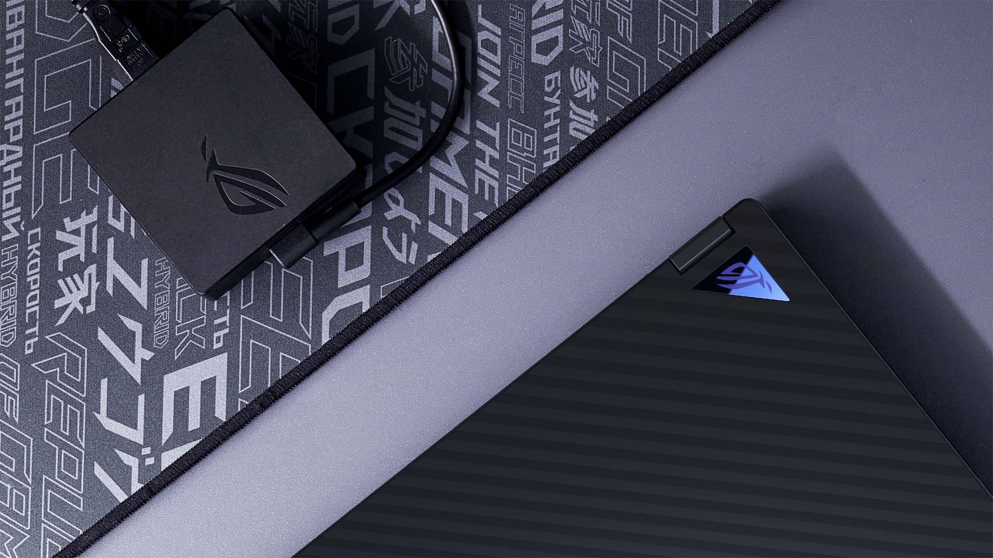 The ROG Flow X13 sitting on a desk, with the wave texture and triangular badge visible, next to a charger with the ROG logo stamped on it.