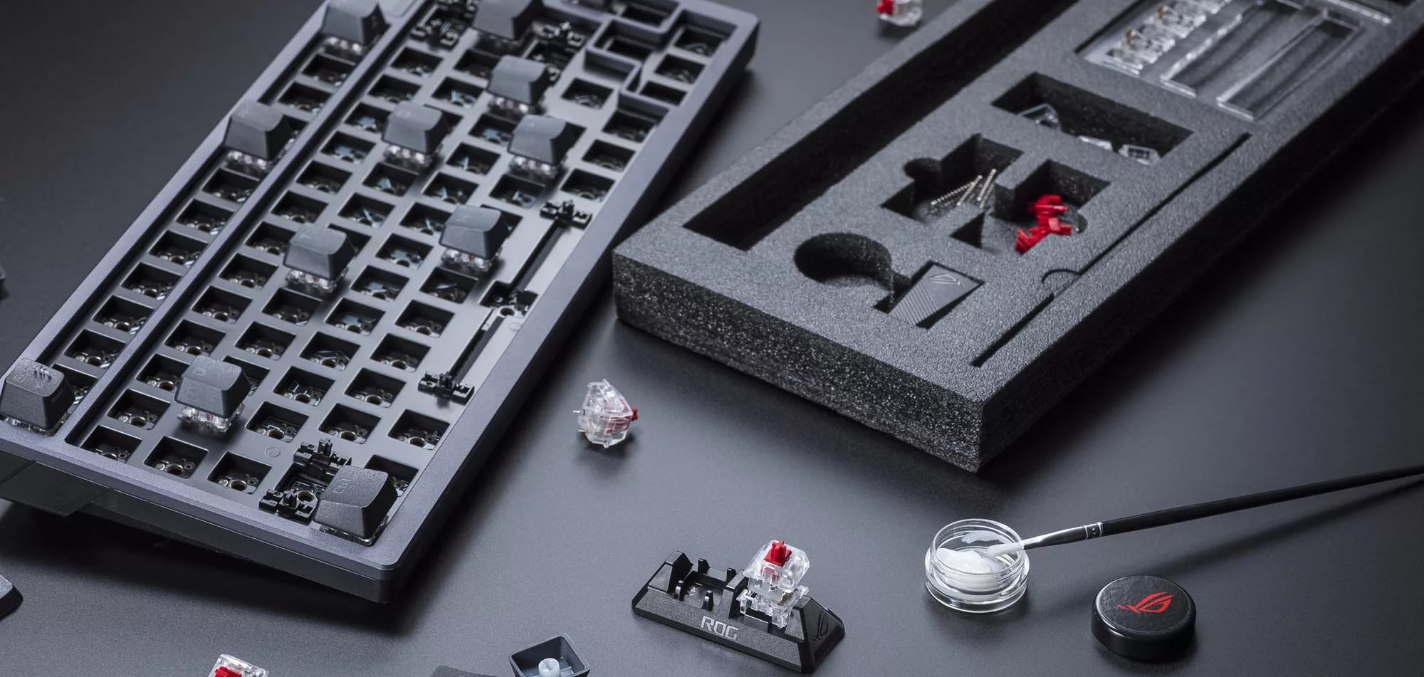 Eine zerlegte ROG Azoth-Tastatur neben einer in Schalterschmiermittel getauchten Bürste.