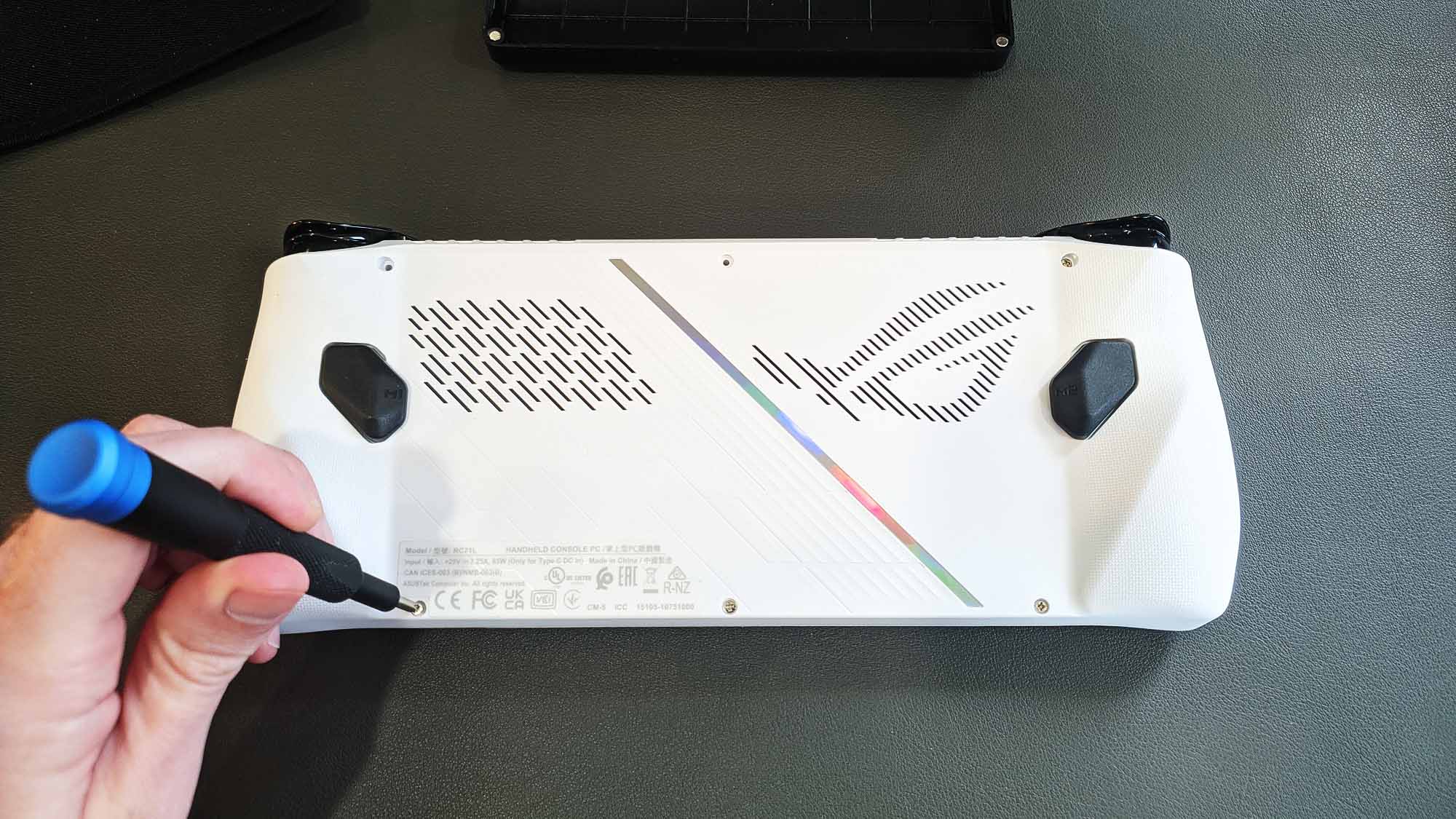 The back side of the ROG Ally, with a hand unscrewing one screw.