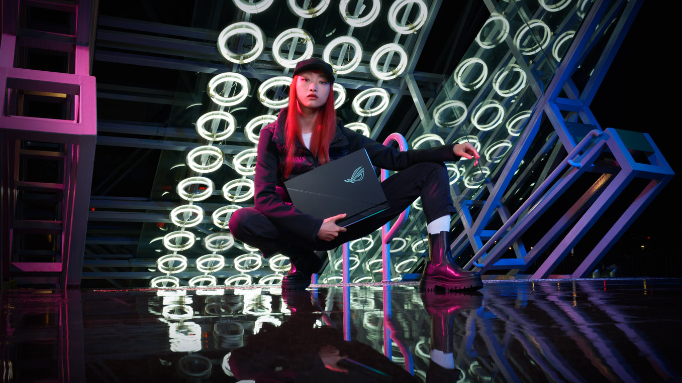 A woman kneeling with a Strix SCAR laptop in her hands under an array of circular lights.