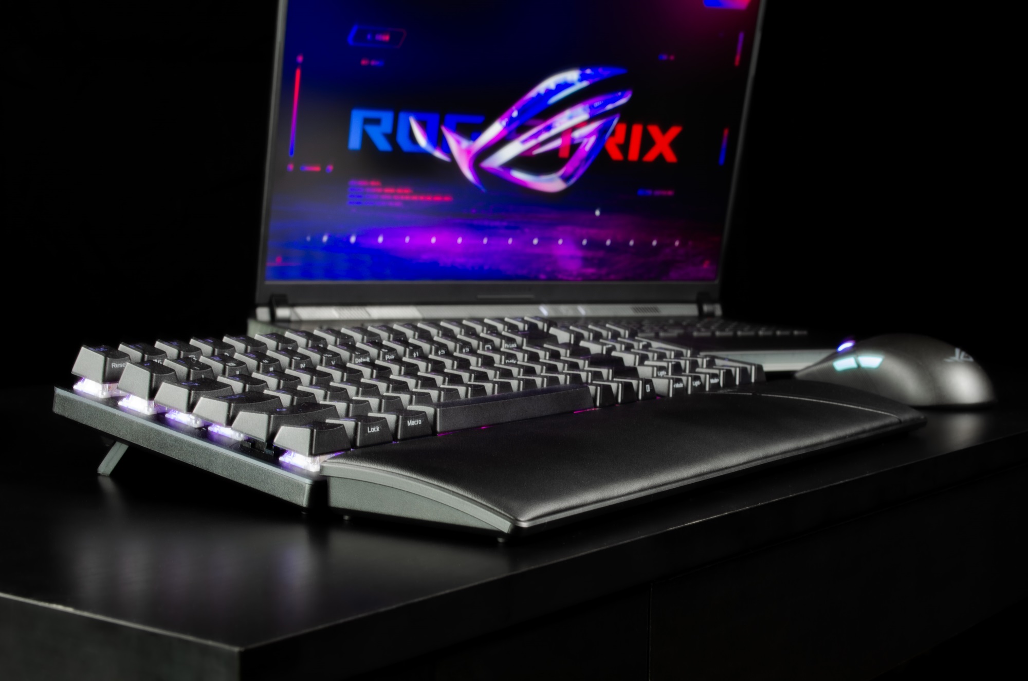 A side view of the ROG Strix Scope II 96 Wireless gaming keyboard in front of a ROG mouse and laptop