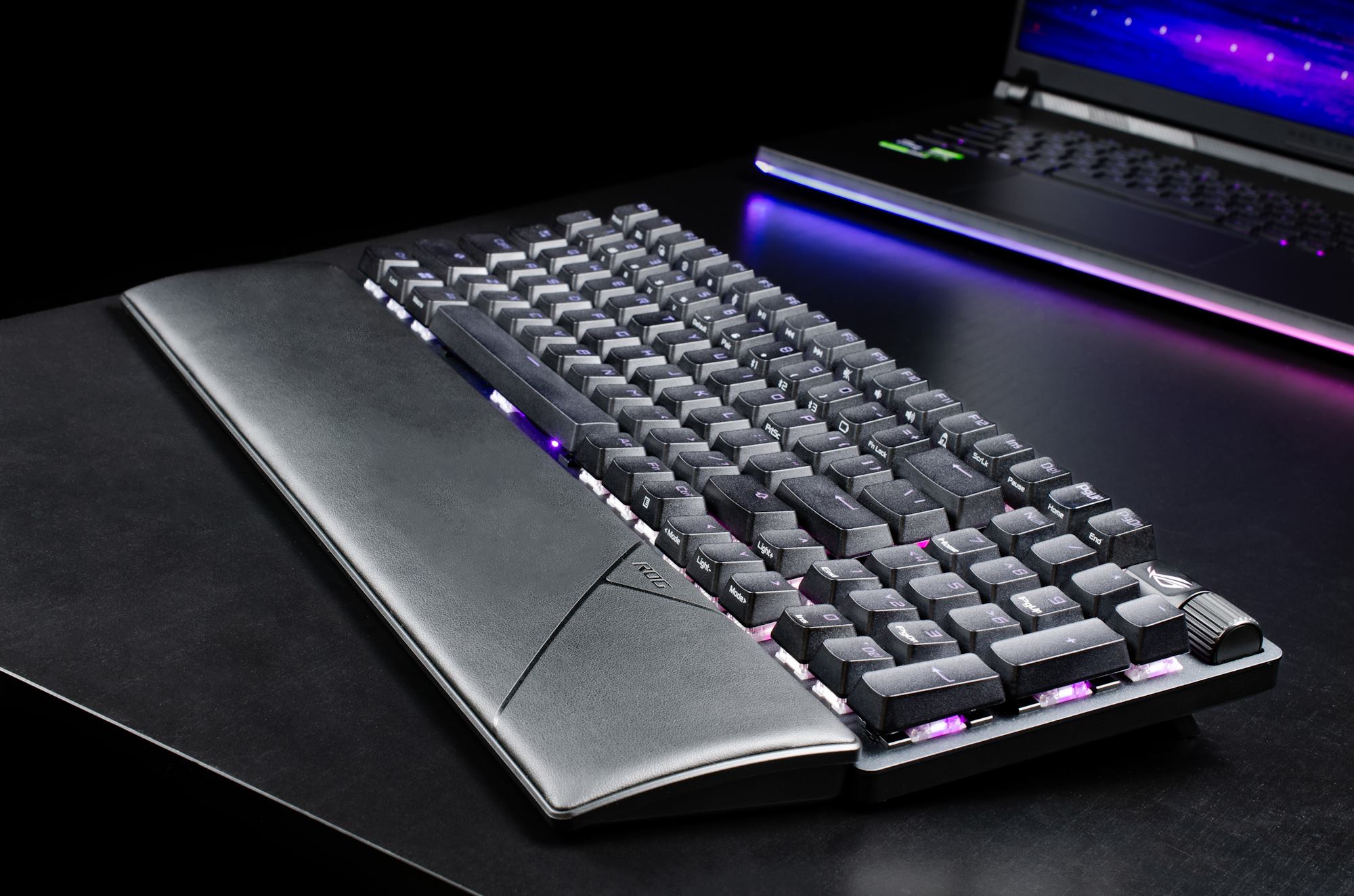 The ROG Strix Scope II 96 Wireless gaming keyboard with its palmrest attached on a table with an ROG laptop