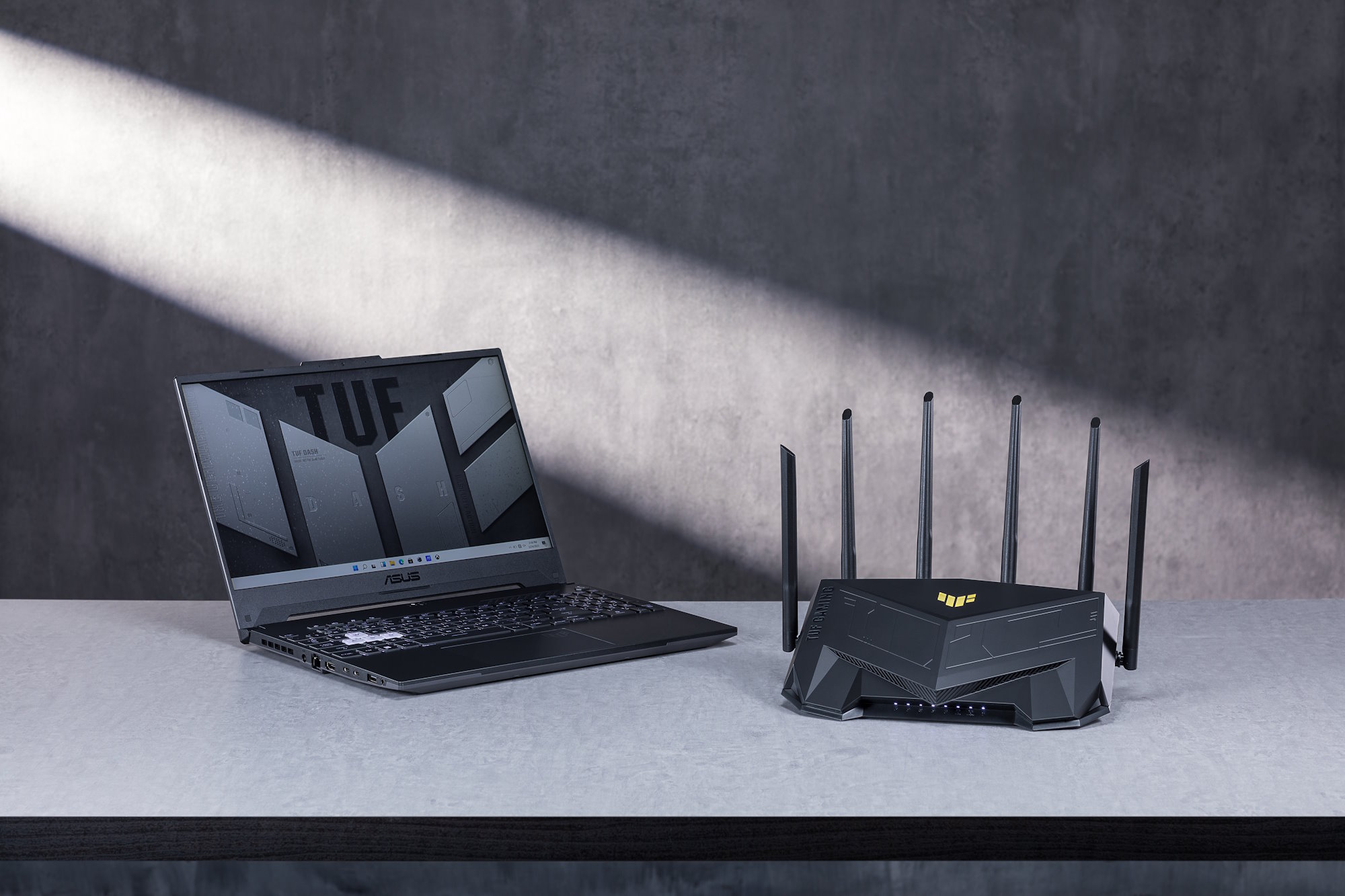 The TUF Gaming AX6000 wirless router on a table with the TUF Gaming A15 laptop