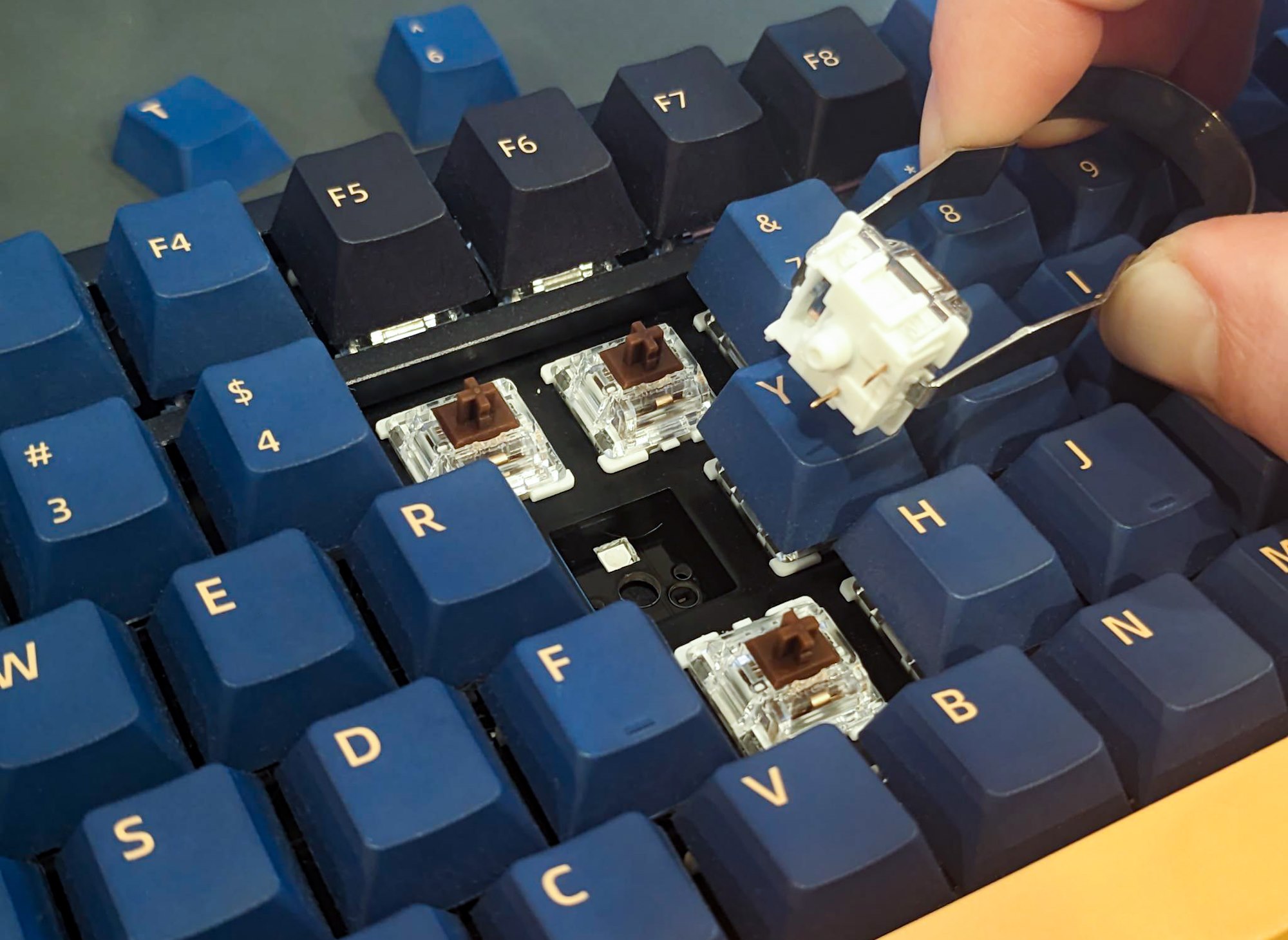A person holding a removed switch using the switch puller included with the ROG Azoth keyboard