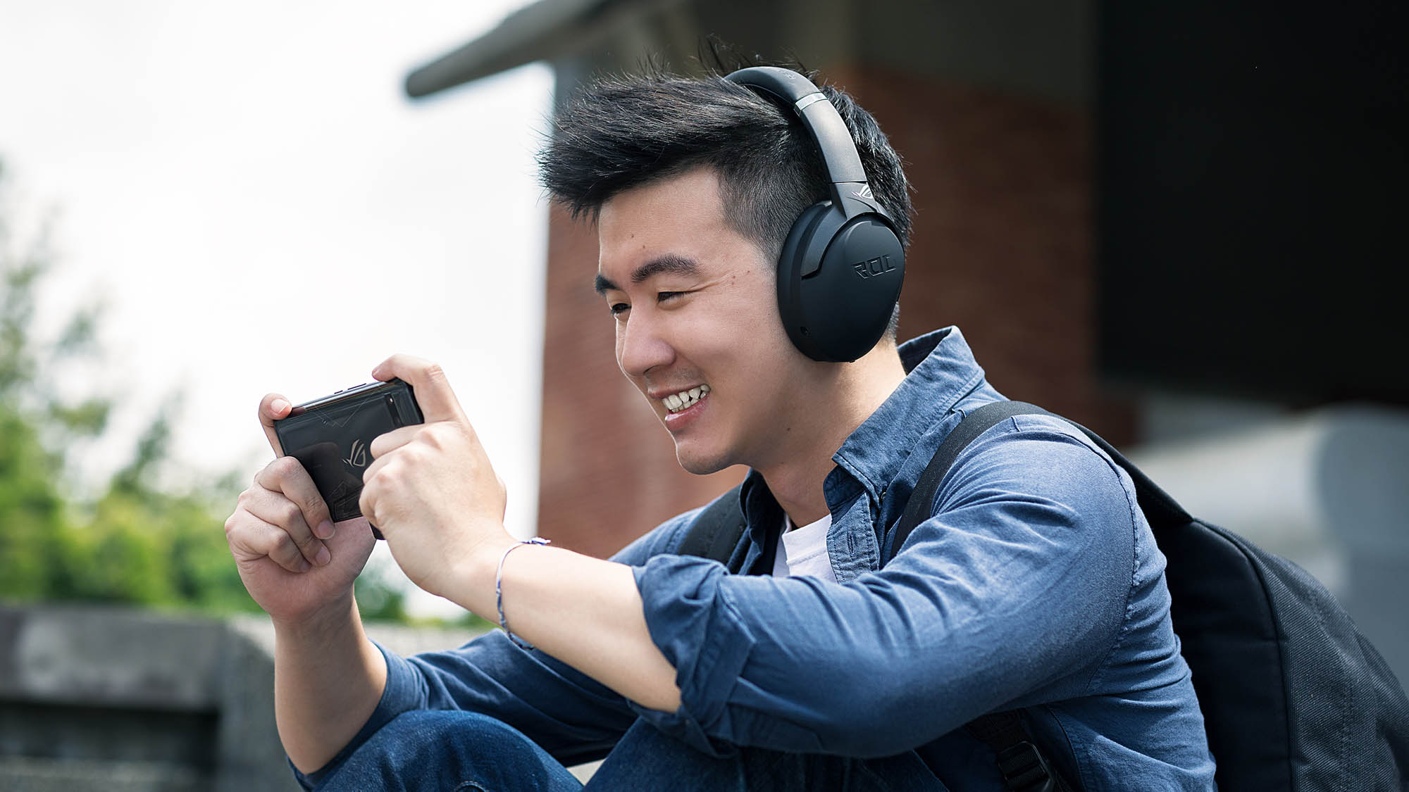 A man playing games on his phone wearing a black ROG Strix Go headset.