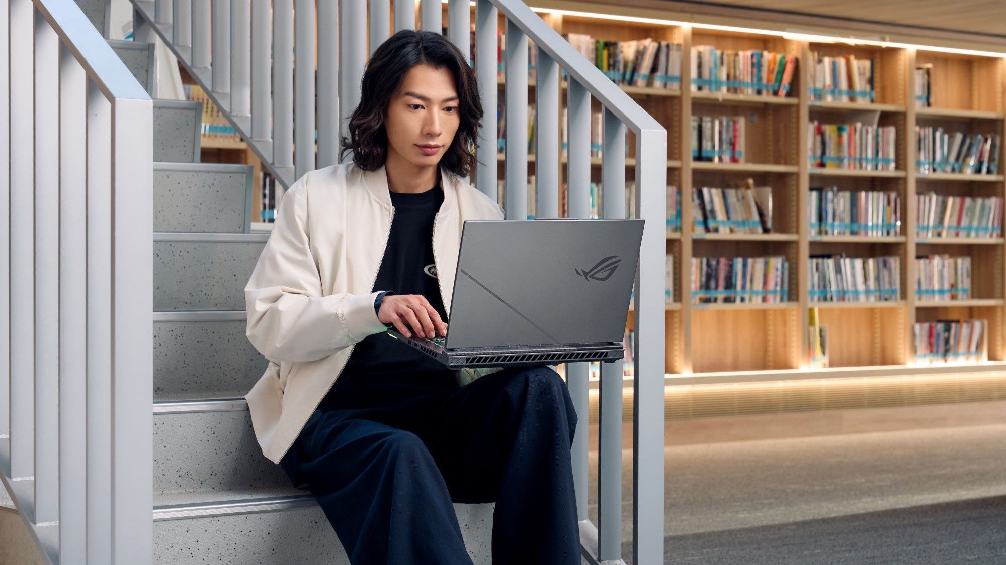 A man holding an ROG Strix G16 laptop in a library.