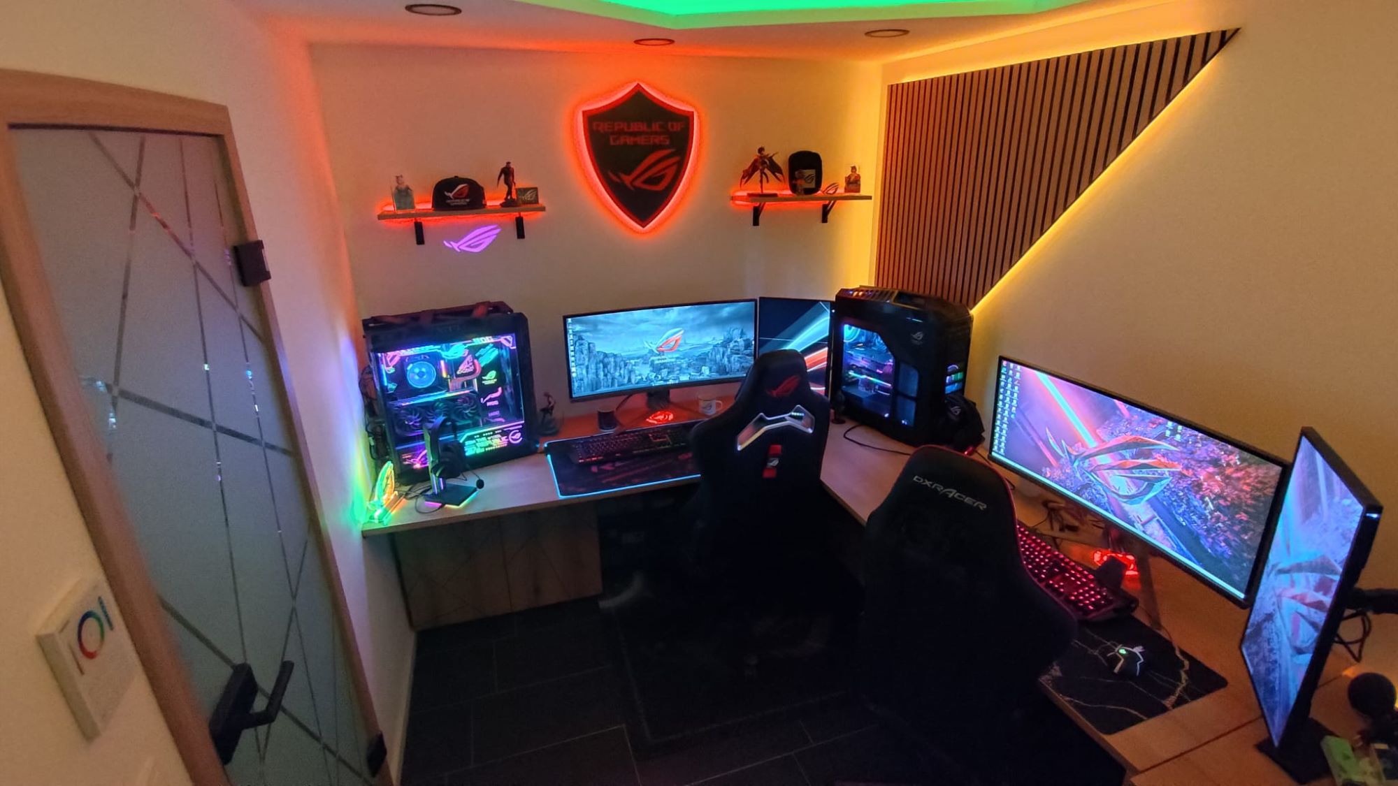 A room filled with ROG gear and logos, including a glowing red ROG wall-mounted plaque and multiple ROG desktop PCs.