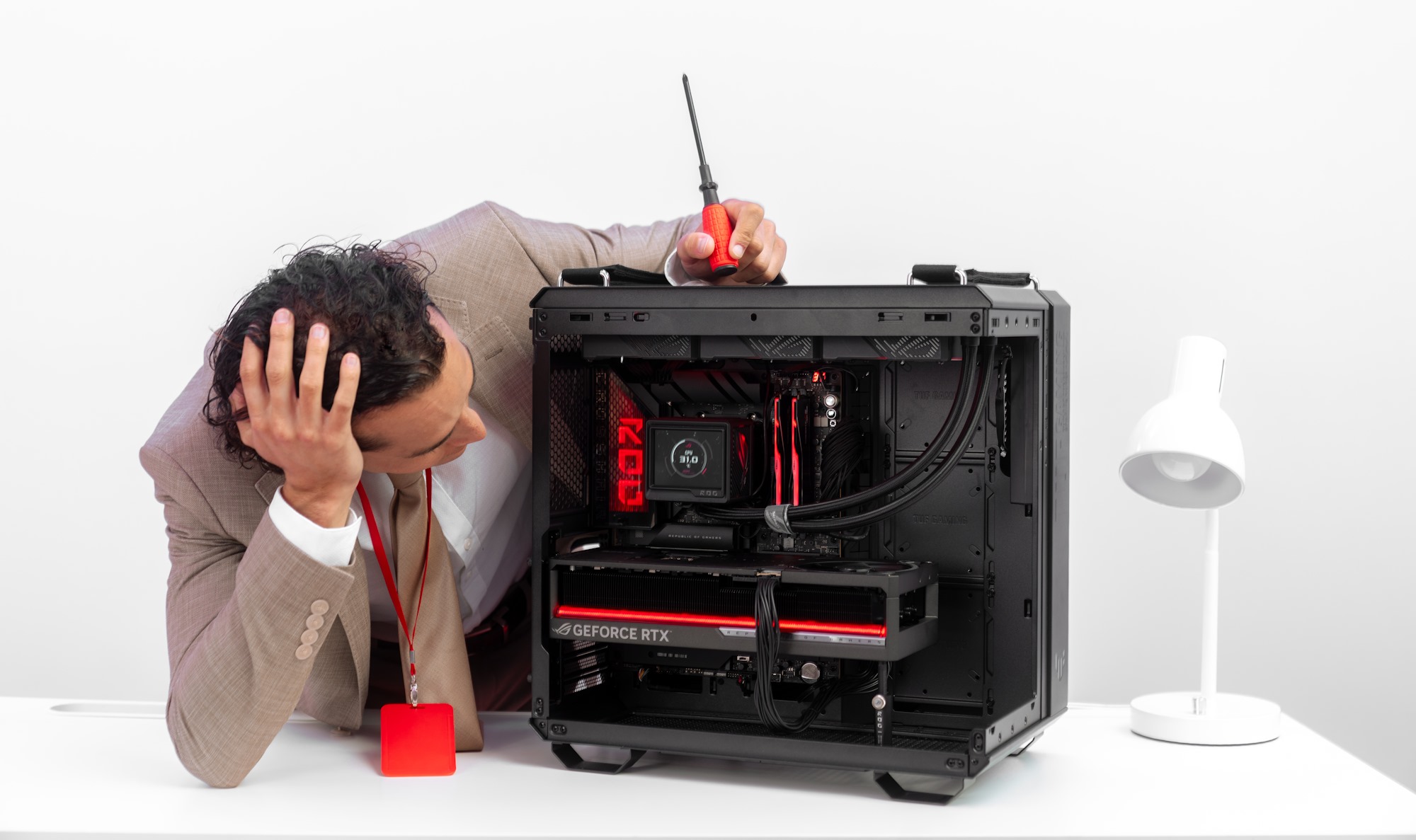 A man leans over to look inside the chassis of a completed PC build, one hand on his forehead and the other holding a screwdriver