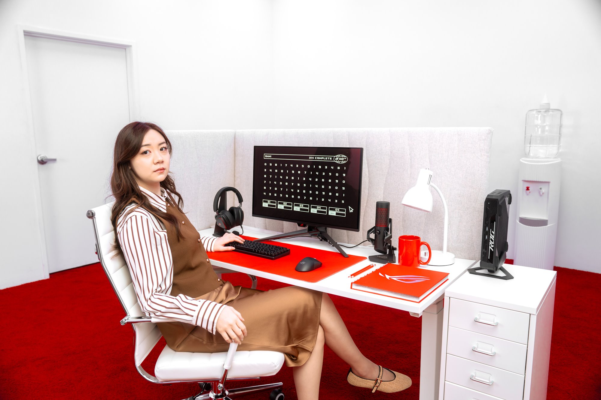 A woman leans back in her chair while sitting at an office cubicle desk full of ROG gear