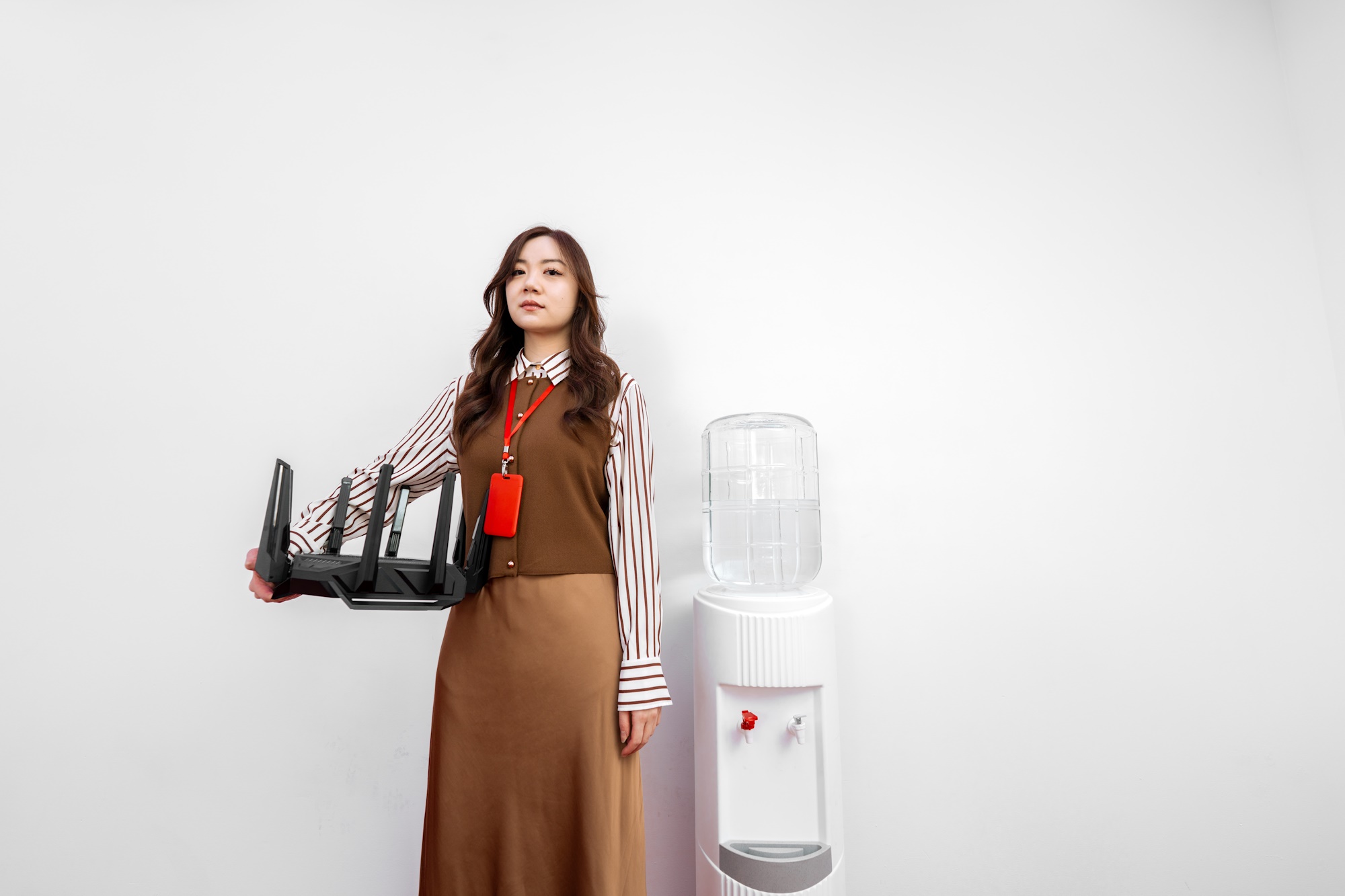 A young woman stands by a water cooler, holding the ROG Rapture GT-BE98 Pro wireless router with one hand