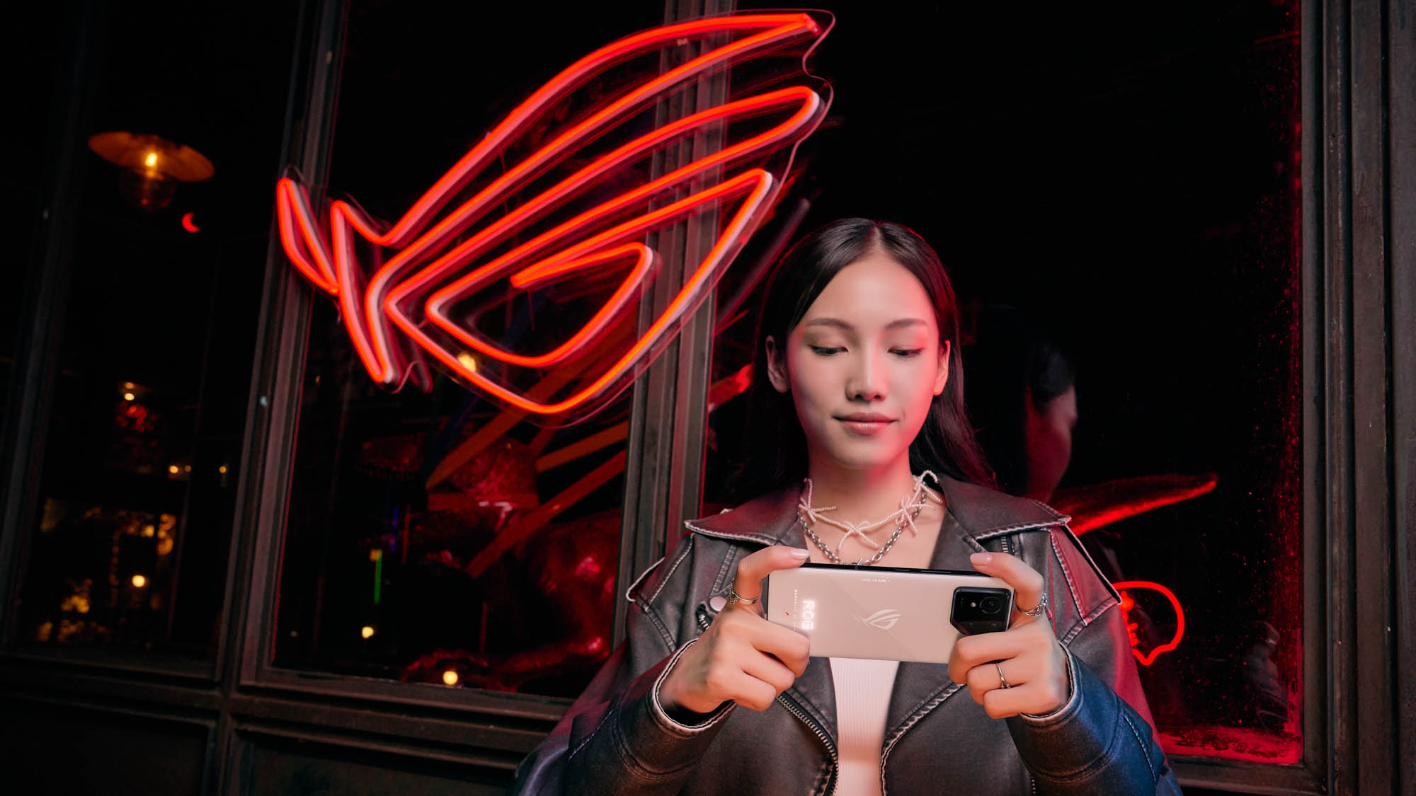 A woman playing games on an ROG Phone in front of a neon sign