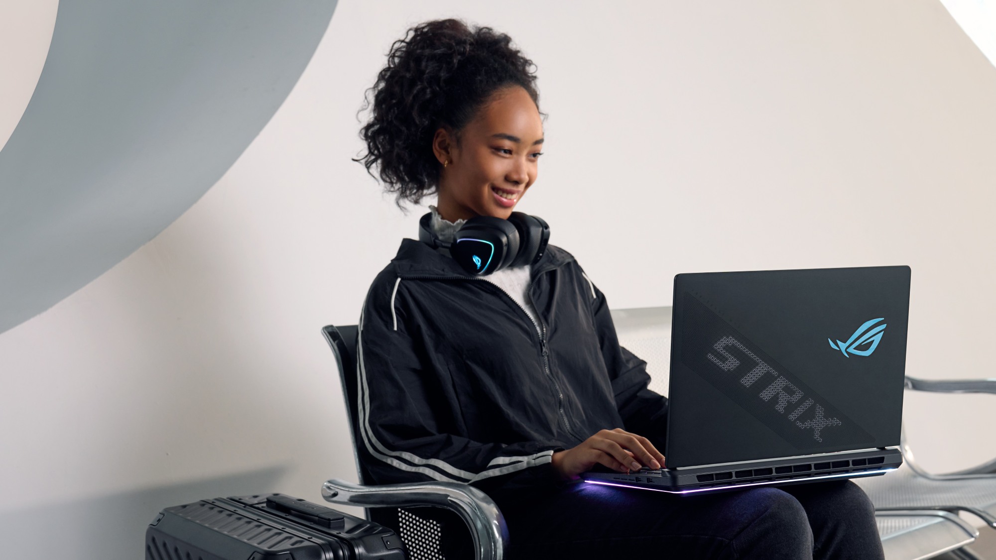 A woman sitting on a bench with an ROG Strix SCAR laptop and headphones around her neck