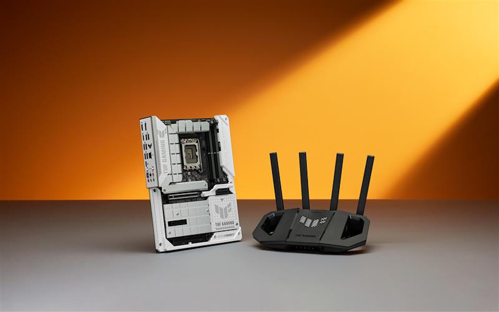 The TUF Gaming BE3600 gaming router on a flat surface close to a TUF Gaming motherboard against an orange background