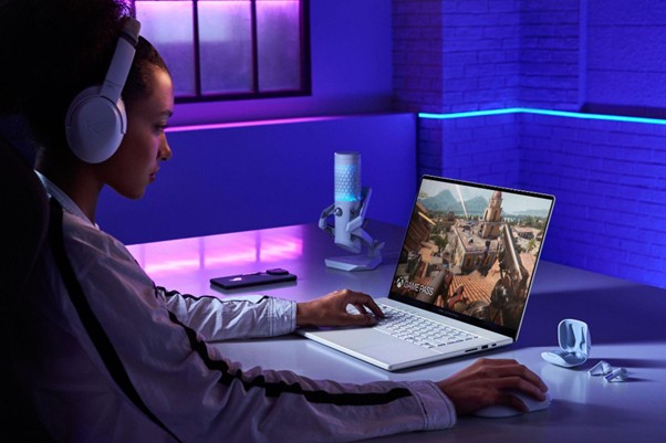  Mulher com fones de ouvido usando notebook para explorar o metaverso em ambiente com iluminação azul e roxa.