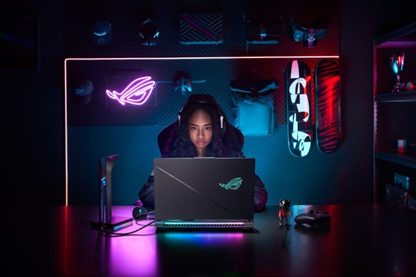 Mulher com headset e notebook, em espaço de gaming com luzes neon, relacionada ao metaverso.