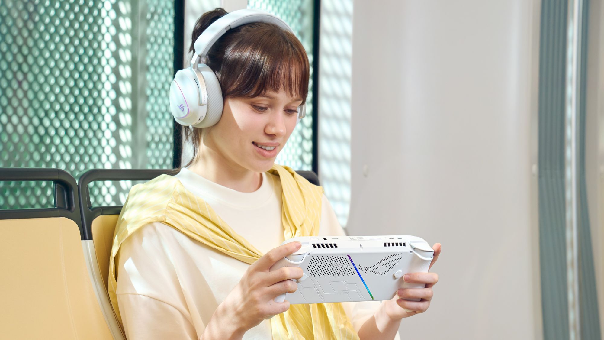 A woman sits on a couch playing an ROG Xbox Ally while wearing an ROG headset