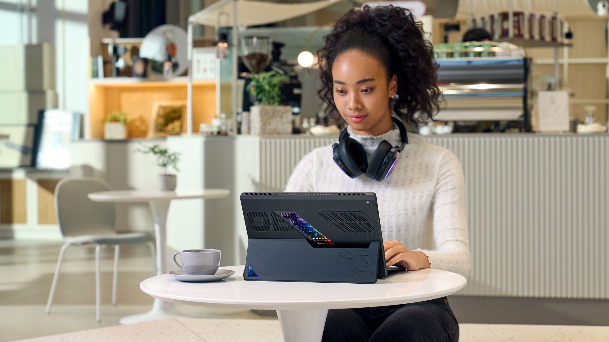 Một người phụ nữ tại quán cà phê đang nhìn vào chiếc ROG Flow Z13 trên bàn.