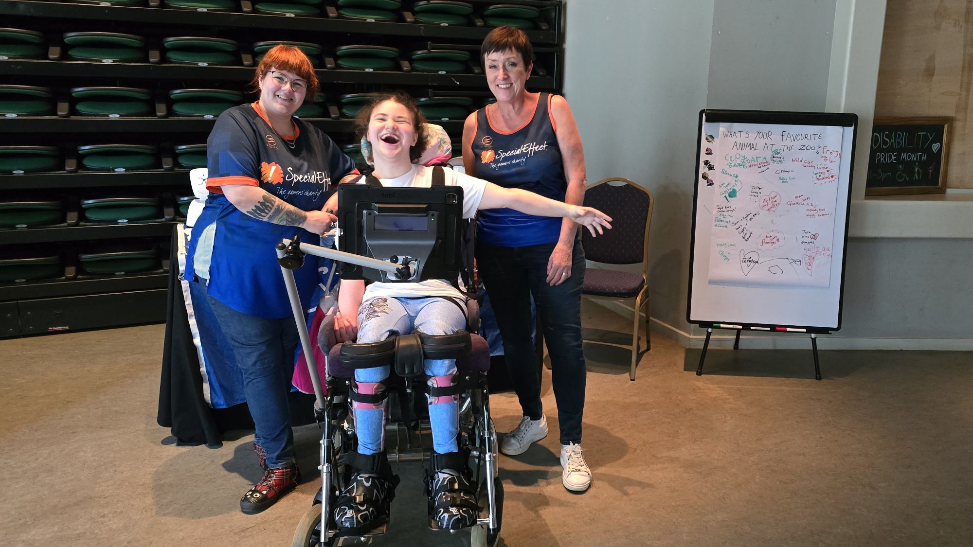 Two woman standing with another woman in a wheelchair laughing.